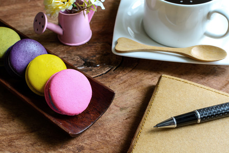 Colorful macaroons and a cup of coffee with notebook on wooden tableの写真素材