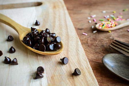 Chocolate chips on wooden spoon and ingredients for cooking dessertの写真素材