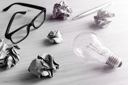 Crumpled paper balls with eye glasses and pen on wooden desk, creative writing conceptの写真素材