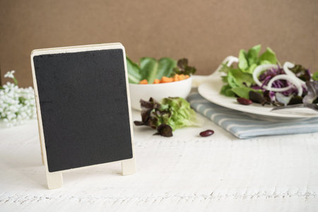 Blank blackboard with salad on white wooden table with copy space