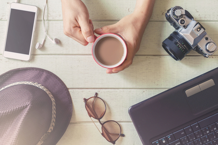 Laptop and cup of coffee on wooden desk with hand holding a cup of coffee, Top viewの写真素材