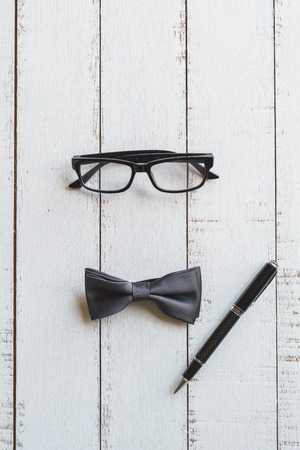 Glasses, black bowtie and pen on white wooden background, Top viewの写真素材