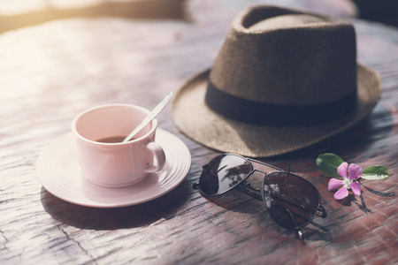 hat with sunglasses and cup of coffee on wooden tableの写真素材