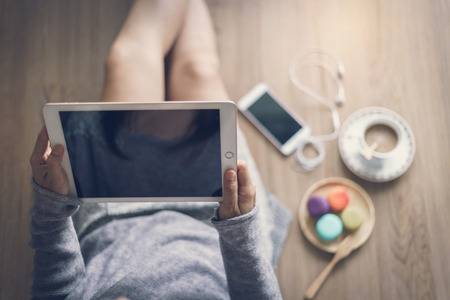 Young woman relaxing at cozy home atmosphere on the wooden floor with cup of coffee and macaroon. Soft focusの写真素材