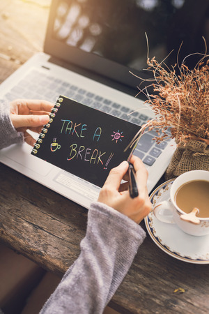 Young woman working by using a laptop with coffee and flower. Take a break note in handsの写真素材