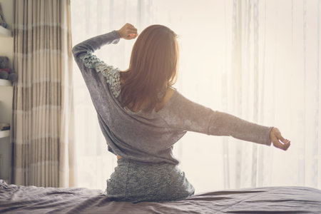 Woman stretching arms and waking up sitting on the bed in the morning at homeの写真素材