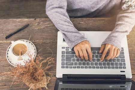 Young woman working by using a laptop on wooden table with coffee and flower. Hands typing on a keyboardの写真素材