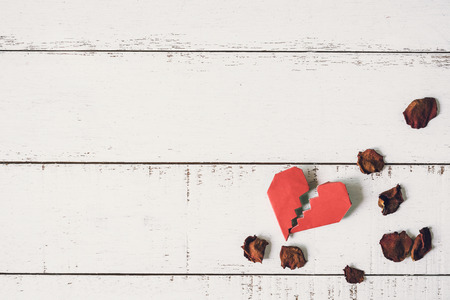 Red broken heart with dried rose petal on white wooden backgroundの写真素材