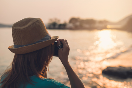 Young woman traveler taking photo on the beach at beautiful sunsetの写真素材