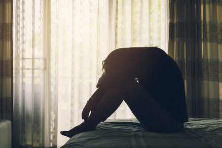 Woman Suffering From Depression Sitting On Bed in the dark bedroomの写真素材