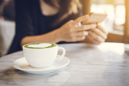 Young asian woman using mobile phone and texting in social networks with cup of matcha latte green teaの写真素材