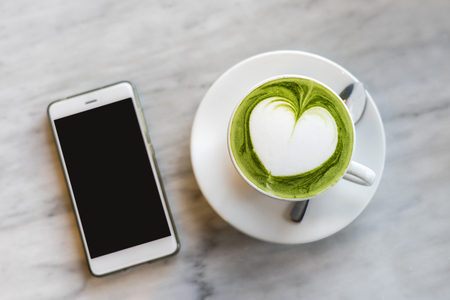 Cup of green tea matcha latte with smart phoneの写真素材