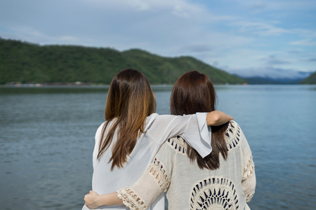 Two young women friends relaxing on wooden pier and looking at the natureの写真素材