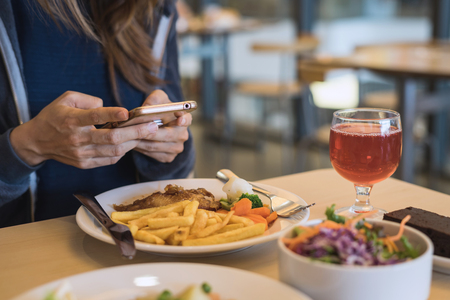Young woman using an application in her smartphone while eatingの写真素材