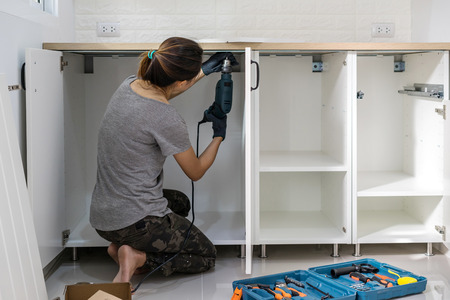 Young woman using electric screwdriver to installation kitchen furniture, DIY conceptの写真素材