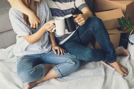 Young happy couple moving in new home, sitting and relaxing on the floor with cardboard boxesの写真素材
