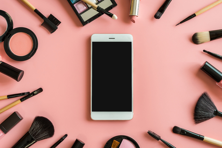 Set of make up brushes and cosmetics on pink background with smart phone and copy spaceの写真素材