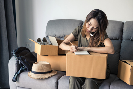 Young asian woman working online business by using smart phone and checking customer orders at home, Online business owner conceptの写真素材