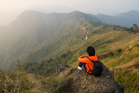 Young traveler sitting and looking at beautiful landscape on top of mountainの写真素材