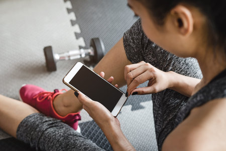 Young asian sportswoman sitting and using smartphone in gym