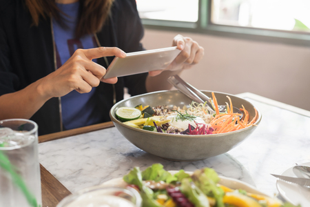 Young woman taking photo of food with smart phone in restaurantの写真素材