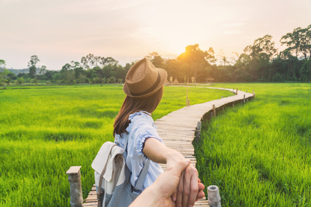 Young woman traveler holding man's hand and leading him on green paddy field, Couple vacation travel conceptの写真素材