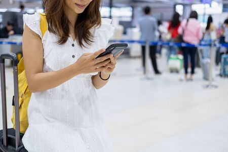 Young woman traveler using her smartphone to check flight in the airportの写真素材