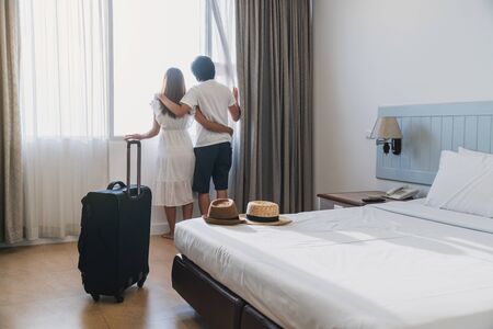Young couple traveler with luggage looking at view in hotel room on summer vacationの写真素材