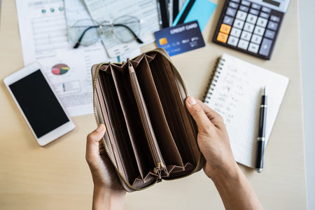 Stressed young woman open her empty wallet and calculating expenses at home