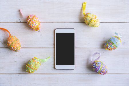 Colorful easter eggs on wooden background with smartphone, Top viewの写真素材