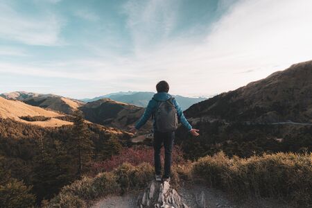 Young traveler standing and looking at beautiful landscape on top of mountainの写真素材