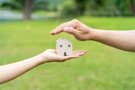 Close-up of couple hand holding wooden house model with green natural and sunlight backgroundの写真素材