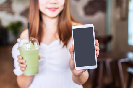 Young female showing an empty screen smart phone with copy space while enjoying a drink in a coffee...