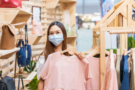 Young Asian woman wearing surgical mask shopping in clothes stores at the mall, New normal and lifestyle conceptの写真素材
