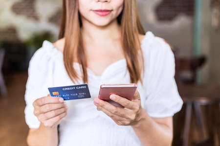 Young woman holding a credit card and using smartphone for making online payment shopping in restaurantの写真素材