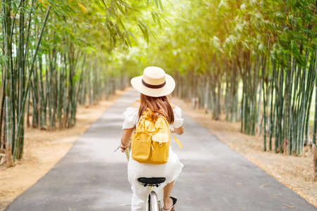 Young happy woman enjoying and riding a bicycle in the bamboo forest while traveling in summerの写真素材