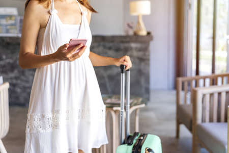 Young woman with baggage using smartphone while waiting to check in the tropical resort, Travel lifestyle conceptの写真素材