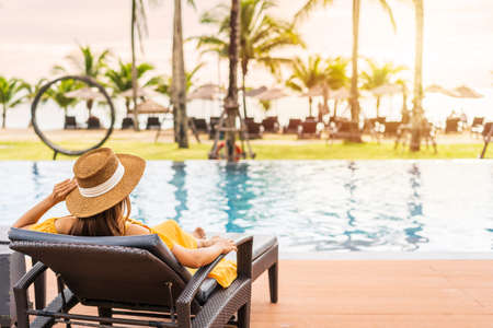 Young woman traveler relaxing and enjoying the sunset by a tropical resort pool while traveling for summer vacationの写真素材