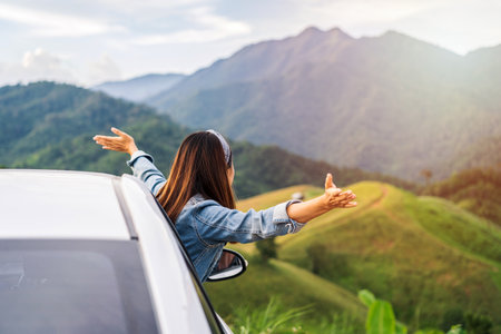 Young woman traveler sitting in a car watching a beautiful mountain view while travel driving road trip on vacationの写真素材