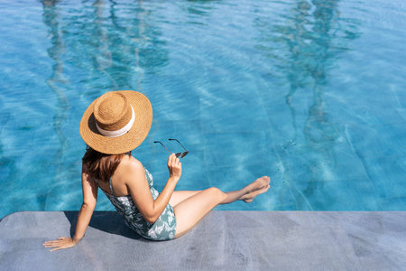 Young woman traveler relaxing and enjoying by a tropical resort pool while traveling for summer...