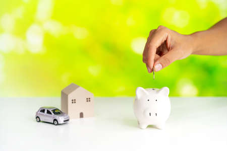Hand put coins into the piggy bank with green nature background, Saving money for house and car conceptの写真素材