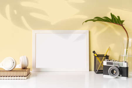 Modern and stylish workspace with white frame mock up and desk office supplies and retro camera with color background and copy spaceの写真素材