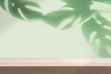 Empty wooden table with shadow of tropical green leave on color background with copy spaceの写真素材