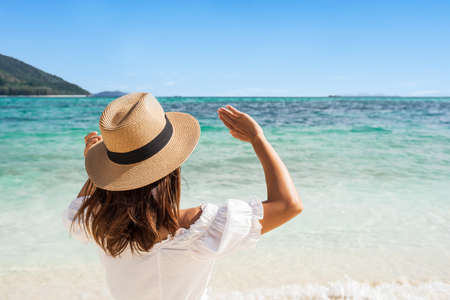 Young woman traveler wearing sunglasses covering face by hand to protect UV rays from the sun at tropical sandy beach on sunny day, Skin care and eyes protect conceptの写真素材