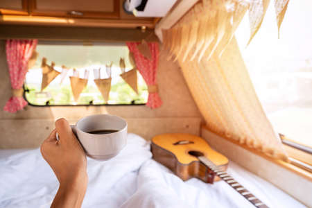 Young woman traveler with cup of coffee laying in camper van and looking beautiful landscape while road trip traveling on vacationの写真素材