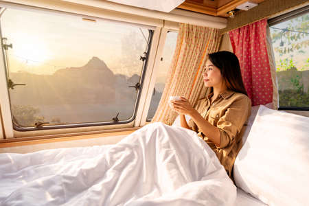 Young woman traveler with cup of coffee laying in camper van and looking beautiful landscape while road trip traveling on vacationの写真素材