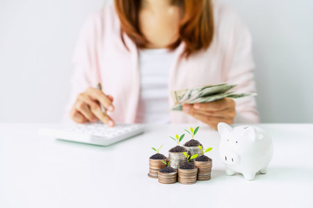 Young woman calculating expenses with stack of coins and piggy bank, Saving money for future investment conceptの写真素材