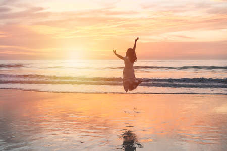 Young woman jumping on the beach at beautiful sunset, Summer vacation conceptの写真素材