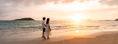Young woman traveler holding man's hand and looking beautiful sunset on the beach, Couple on vacation in summer conceptの写真素材