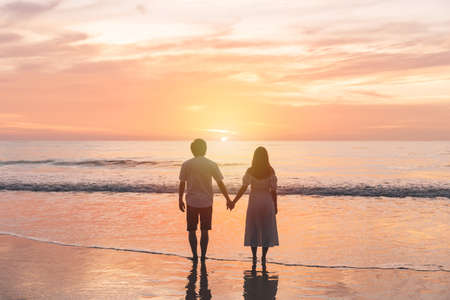 Young Asian couple holding hand together and looking beautiful sunset on the beach, Summer vacation conceptの写真素材